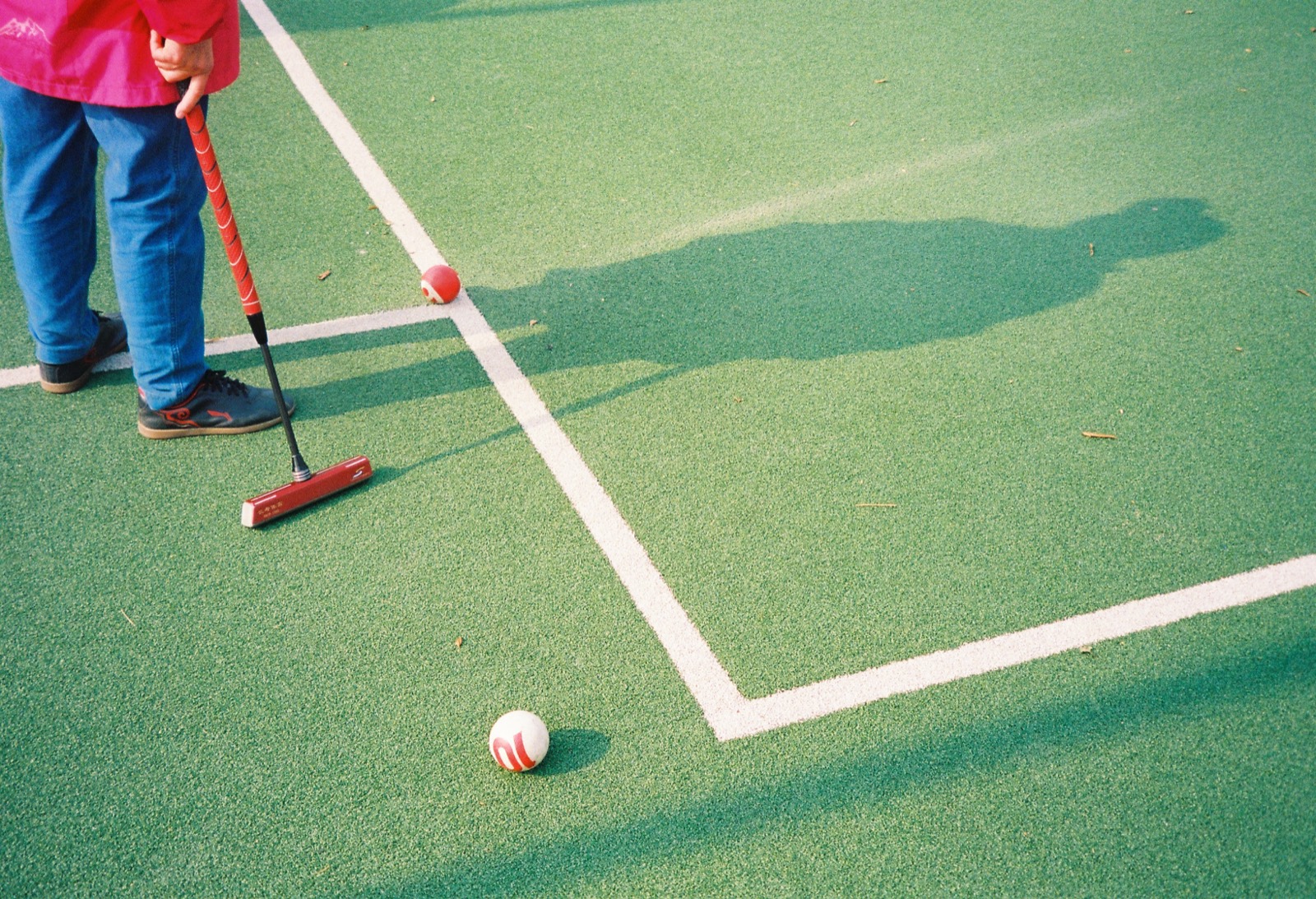 A croquet mallet and long shadow on a green court